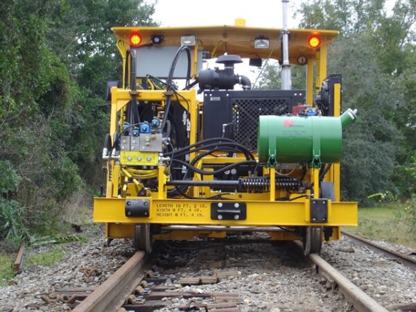A Nordco Curve Gang Spiker from a frontal profile mounted on the rail